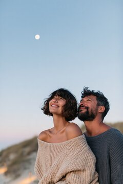 Portrait of a smiling couple under the moon at twilight on a sandy beach for vertical mobile wallpaper and romantic poster design