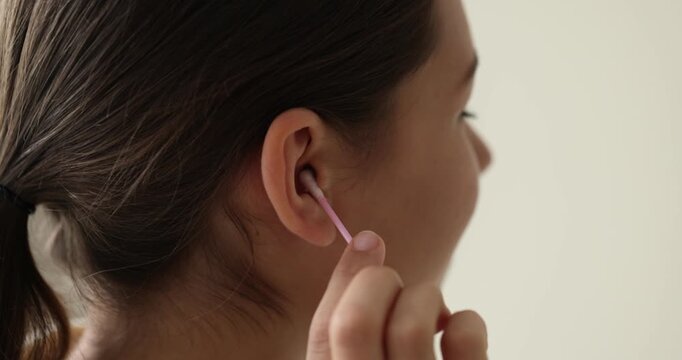 Teenage girl cleaning ear with cotton swab indoors, closeup