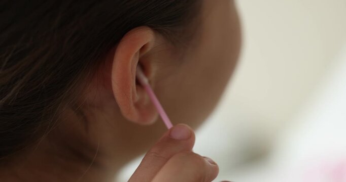 Teenage girl cleaning ear with cotton swab indoors, closeup