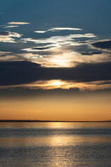 Fototapeta premium atmospheric sunset view over Lake Constance (Bodensee) taken from the Austrian shore in Bregenz, featuring golden sunlight breaking through dramatic cloud layers and reflecting gracefully across the c