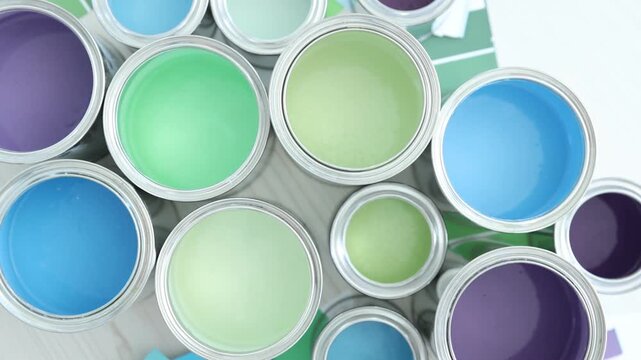 Metal cans with different colorful paints, brush and color palettes on white wooden table, flat lay. Camera spinning