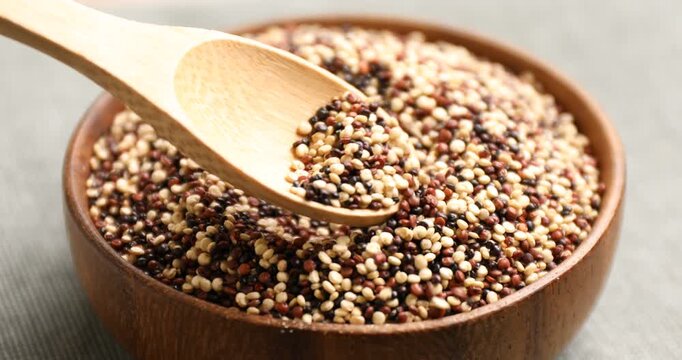 Taking raw mixed quinoa with spoon from bowl at light table, closeup