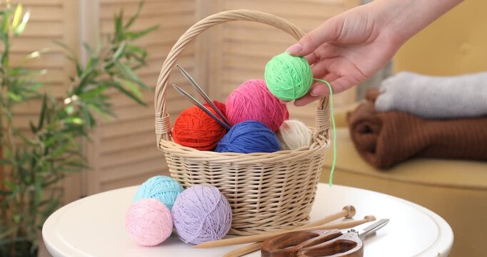 Woman putting knitting yarns into wicker basket indoors, closeup