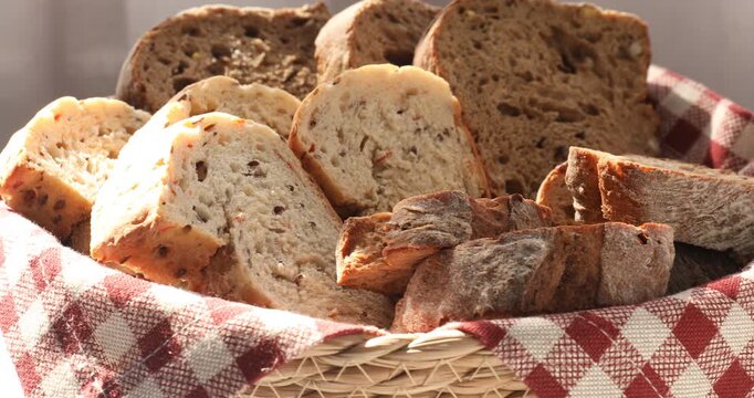 Different types of bread in wicker basket on table indoors, closeup
