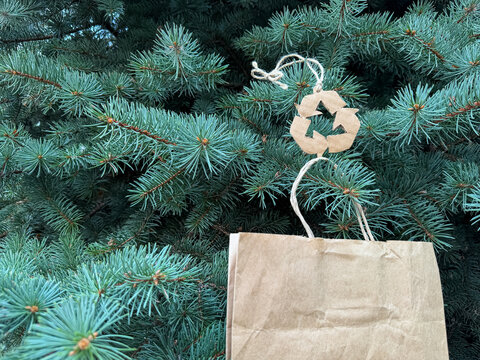 Paper bag with eco recycling symbol hanging on lush fir tree, green gift delivery, christmas celebration