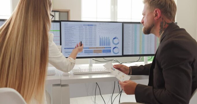 Accountant woman and man at computer monitors. Colleagues in an office review data dashboards and reports, comparing spreadsheets and charts. Concepts include teamwork finance data analysis.