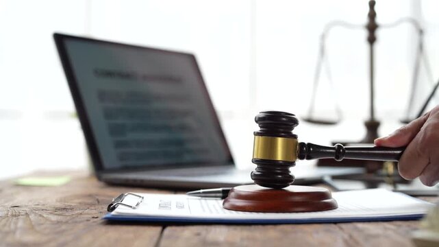 Judge hitting gavel on sounding block in courtroom for verdict, with scales of justice and contract agreement on laptop, symbolizing justice, law, and legal authority