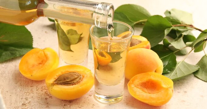 Pouring apricot liqueur into glass, fresh fruits and green leaves at textured table, closeup