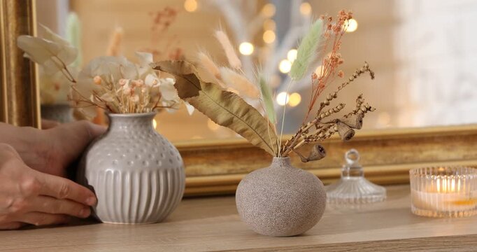 Woman putting beautiful dry flowers in vase onto wooden dresser indoors, closeup