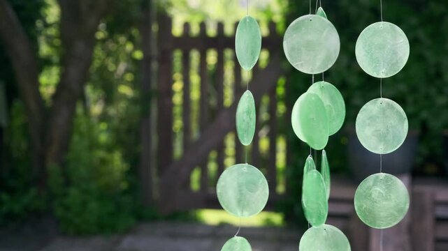An acoustics wind chime mobile with green capiz shells hanging in a sunny garden and moving in the wind	