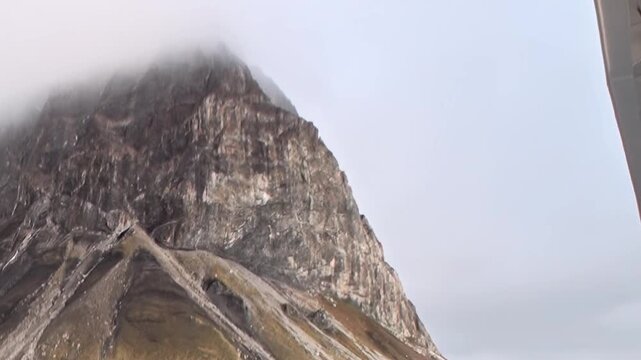 A steep rocky mountain peak rises into fog above the cold coast. The scene also contains close framing, with the framing revealing natural texture and spatial depth.