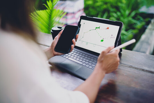 Over the shoulder view Hispanic female developer holding smartphone and electronic stylus pen, analyzing data chart on touch tablet screen during remote freelance project work venue