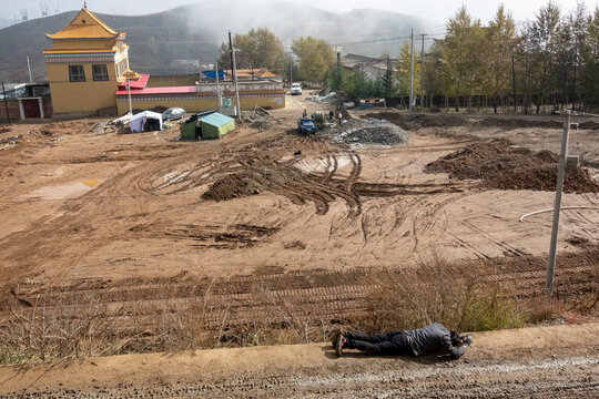 A Tibetan Buddhist pilgrim prostrates on the muddy kora path at Shachong monastery, Qinghai Province, Wayaotai, China