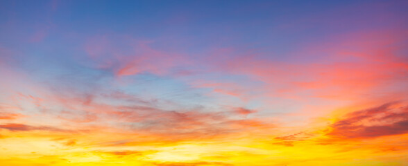 Obraz premium Vibrant Sunset Sky Panorama with Colorful Orange Pink and Blue Clouds,A panoramic photograph capturing a vibrant sunset sky filled with wispy cirrus clouds illuminated in golden yellow, orange, pink, 