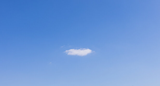 Minimal Single Fluffy White Cloud Floating in Clear Blue Sky,A minimalist photograph capturing a single, small fluffy white cloud floating isolated in a vast, bright blue sky. This clean and peaceful 