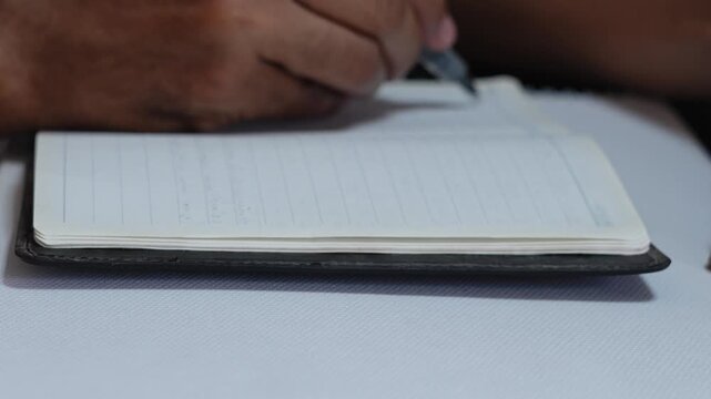 Person's hand writing notes in a lined notebook