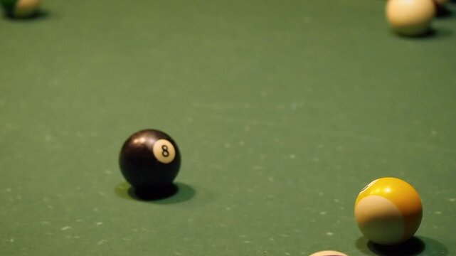A high angle static view of a triangular rack of billiard balls on a green felt surface. A cue ball impacts the rack causing the spheres to scatter across the table. A game of pool