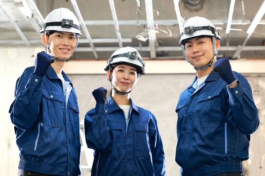 建設現場でガッツポーズをする作業員の男女チーム