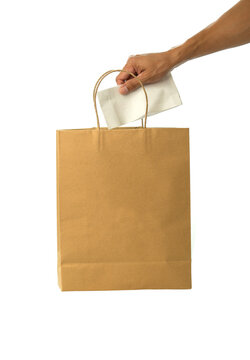 Hand putting white paper packet into brown paper shopping bag isolated on white background