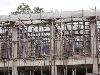 Reinforced concrete building structure under construction, featuring traditional wooden scaffolding, shoring—temporary structures erected to support framework, facilitate worker operations on site  © Vanchuree