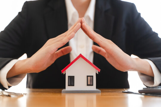Real estate agent or business person protecting small house model with hands, concept of home insurance, property security and financial asset coverage