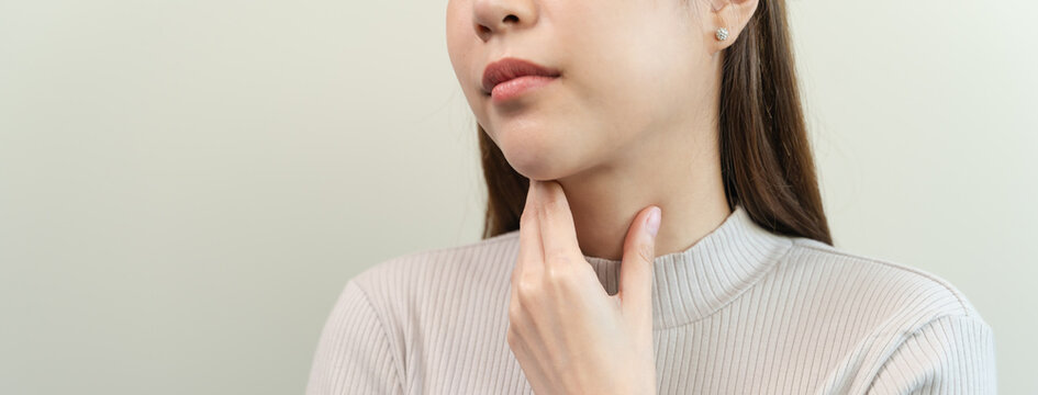 Young Asian woman touching her neck feeling sore throat or thyroid problem, healthcare and medical symptom concept stock photo on light background