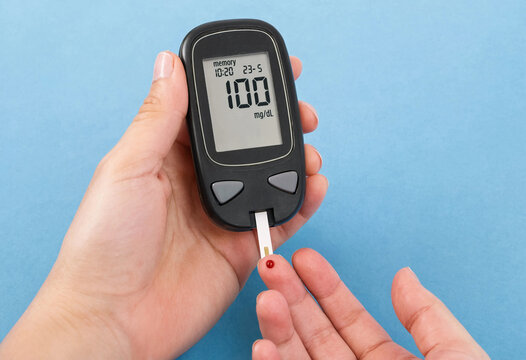 A closeup shot of a person using a portable blood glucose monitor to measure their sugar levels by taking a drop of blood from a fingertip