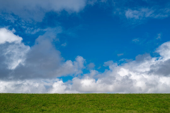 Sky spans the quiet countryside landscape. White clouds drift across the sky. Sky background offers expansive copy space. Rolling meadow meets the blue sky.
