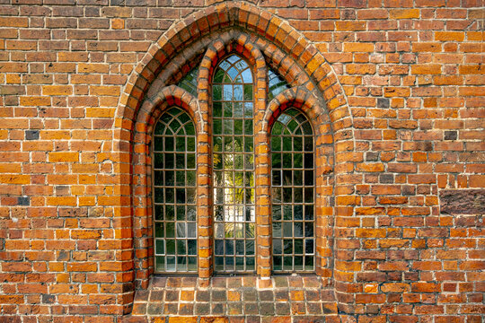 Window in ancient brick building. Window with ornamental Gothic architecture. Antique arched window within rustic wall. Traditional glass window on historic facade.