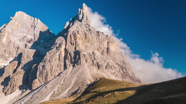 Time lapse: Dramatic view of Cimon della Pala Dolomites, with rugged limestone peaks rising through drifting clouds above alpine slopes under a deep blue sky