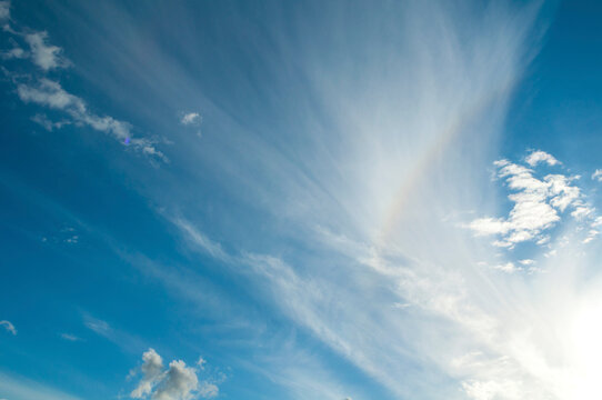 Sunset sky landscape background. Thin wispy cirrus clouds stretching across a blue sky. Soft white streaks radiating from the bright sunlight