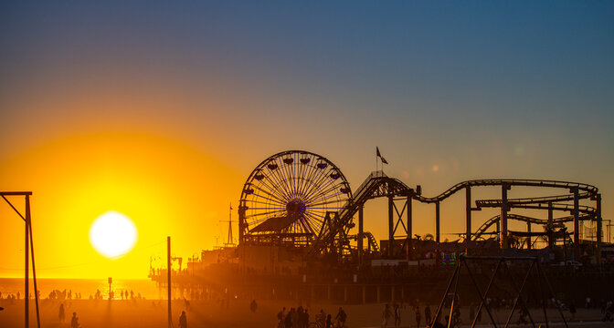 Santa Monica Pier silhouetted at sunset. Golden sunset over Santa Monica Beach. Santa Monica coastline beneath an orange sky. Setting sun beside Santa Monica Pier.