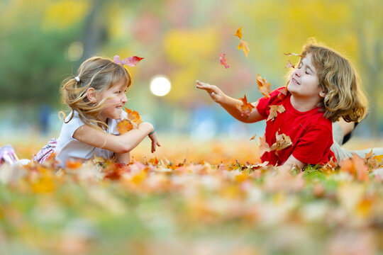 Autumn fun with boy and girl. Children smile beside fallen leaves. Leaves add motion and color. Play looks natural and candid. Laughing kids share outdoor joy. Friendship moment in autumn park.