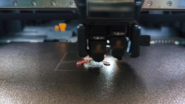 A close‑up of a 3D printer extruder during layer‑by‑layer printing of a small item on the work platform.
