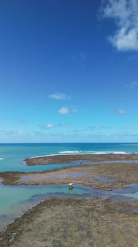 Vista a&eacute;rea de piscinas naturais na mar&eacute; baixa com guarda-sol amarelo isolado, paisagem &uacute;nica e paradis&iacute;aca da Praia do Patacho durante viagem