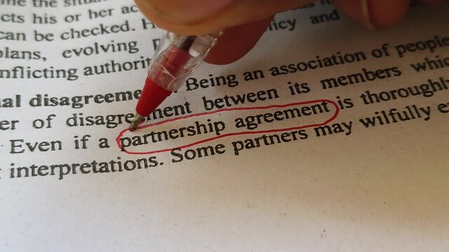 Closeup of hand with red ink pen mark circle around to emphasize or highlight partnership agreement word on legal printed document paper. Bad partnership, contract breach or business dispute concept