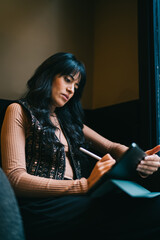 Focused Caucasian female student writing with stylus pen on digital tablet screen in armchair, reviewing online education e-learning course materials assignments and class research © BullRun