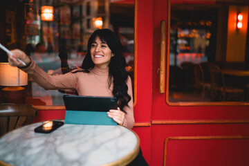 Smiling Caucasian female student pointing stylus pen forward while holding digital tablet at cafe table, presenting online education class coursework e-learning study goals in city © BullRun