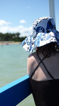 Mulher de chap&eacute;u floral sentada na borda de barco observando o mar durante passeio na Rota Ecol&oacute;gica dos Milagres, cena de viagem relaxante em Alagoas
