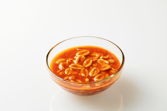 Peanuts in tomato sauce in glass bowl on white background