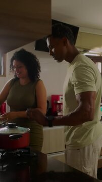 African American man checking simmering pot while Hispanic woman stands beside in kitchen