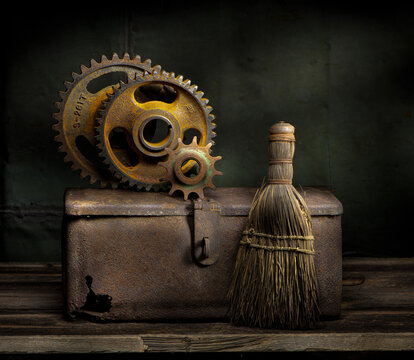 Still life of old rusted gears on old rusted box, with old whisk broom, on wooden table