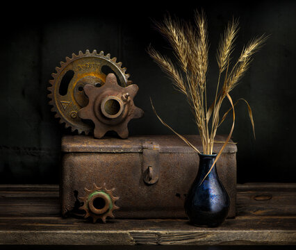 Still life with old rusty gears, rusty box, and wheat stalks in antique vase.