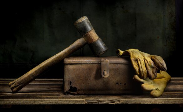 Old hammer and work gloves resting on rusted metal box in vintage still life.