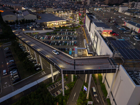Aerial view of the Zama industrial area featuring an elevated road, expansive parking lots, and modern commercial buildings illuminated at dusk in Zama, Kanagawa, Japan.