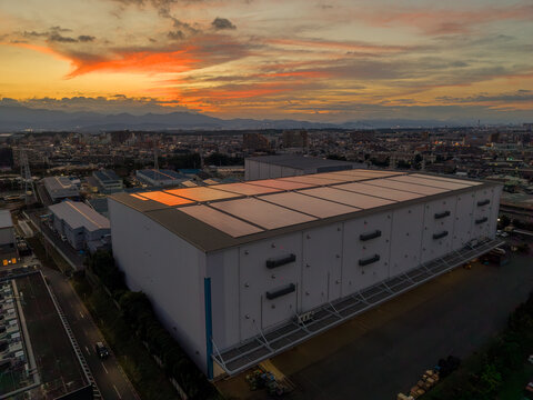 Aerial view of a large industrial warehouse featuring solar panels on its roof at sunset in the Zama industrial area, Zama, Kanagawa, Japan.