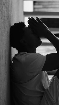African American man holding head against wall in distress in black and white