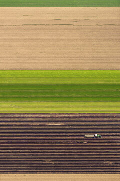 Aerial view of a tractor working in a large agricultural field with distinct rows and colorful soil patterns in El Centro, California, United States.