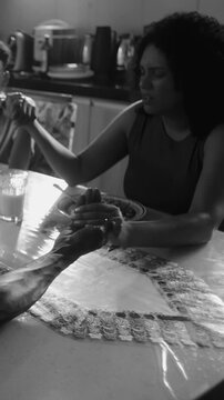 Family holding hands in prayer before meal at dining room table in black and white