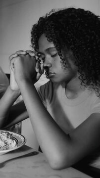 Hispanic teenage girl praying with clasped hands before meal in black and white